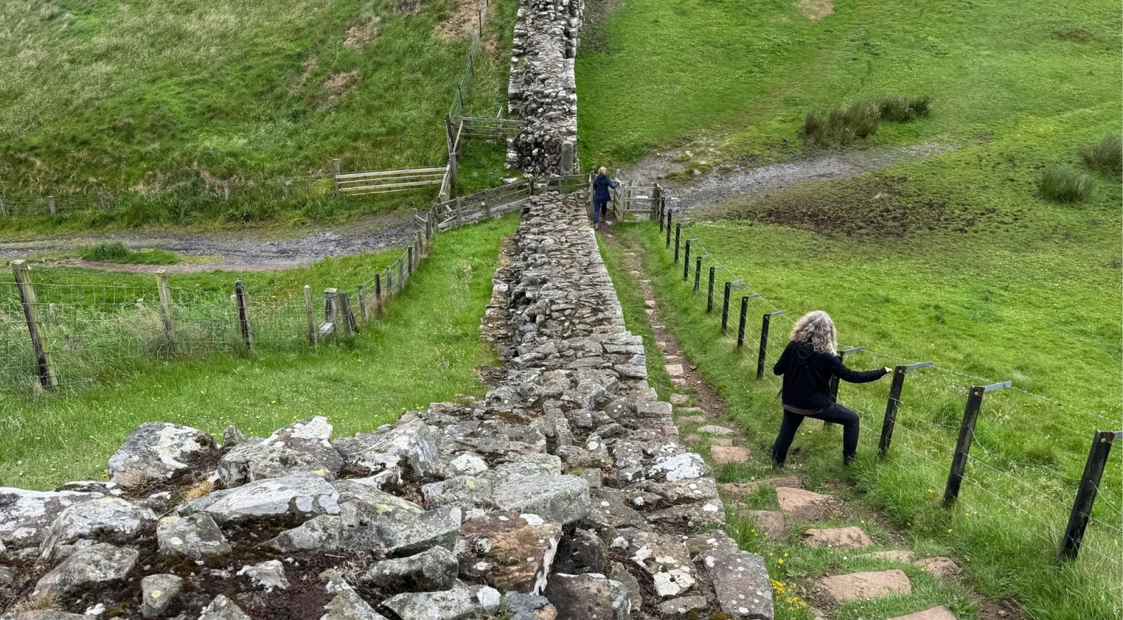 Two walkers on the stone steps of the Hadrian's Wall Path beside the surviving Wall