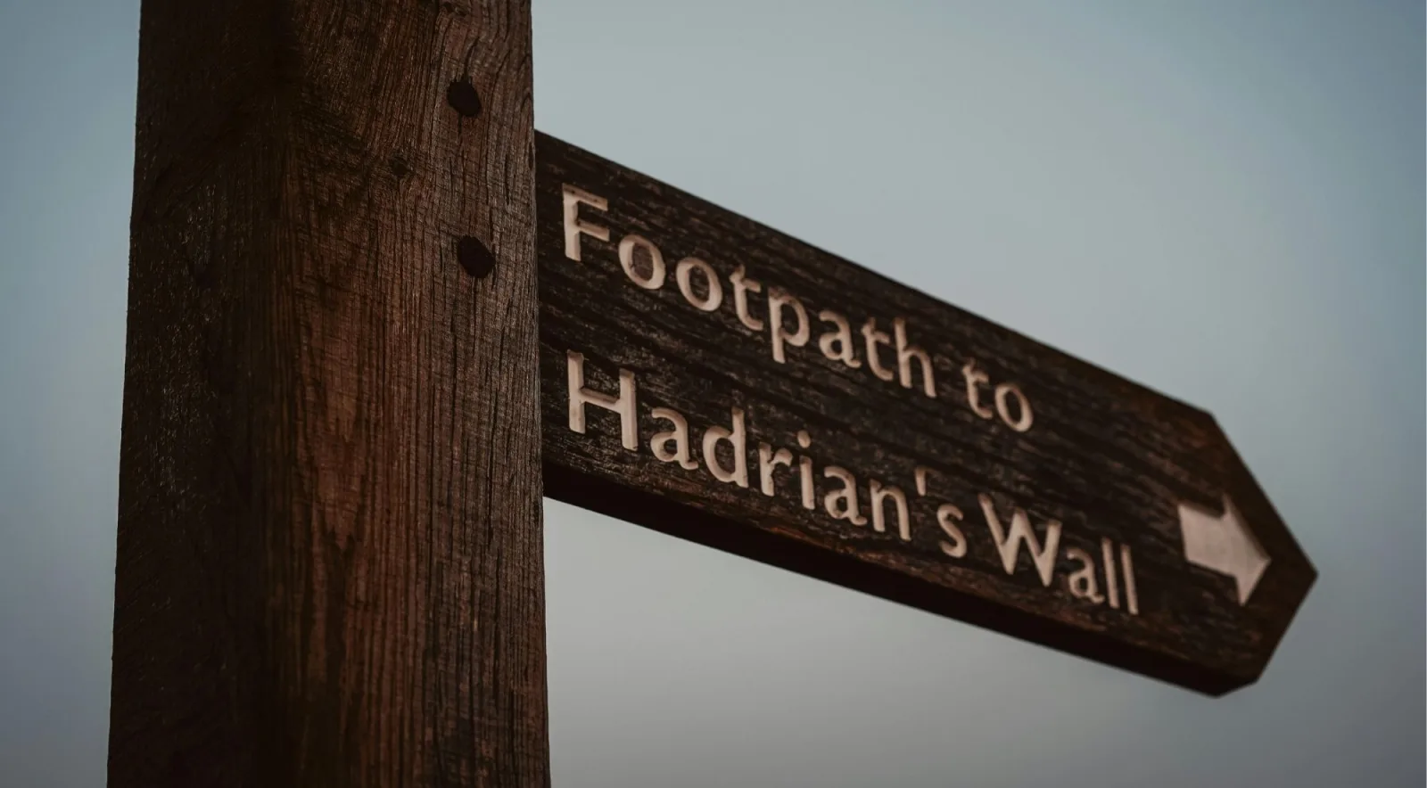 A wooden fingerpost on the Northumberland moor reading Footpath to Hadrian's Wall