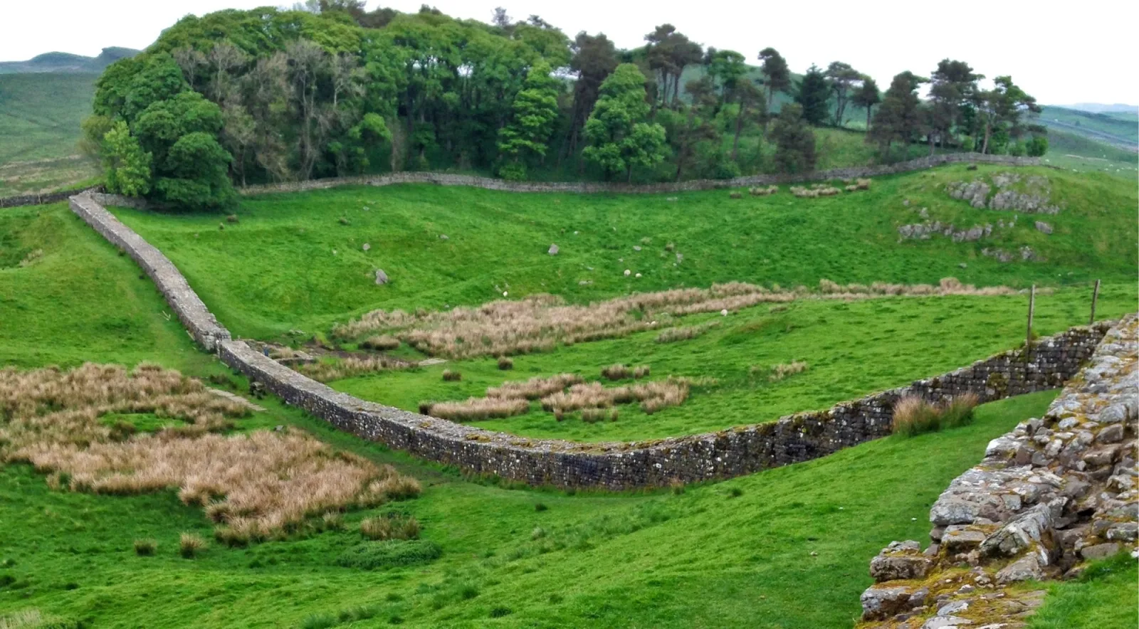 Hadrian's Wall and the Vallum earthwork running down a green hillside in Northumberland