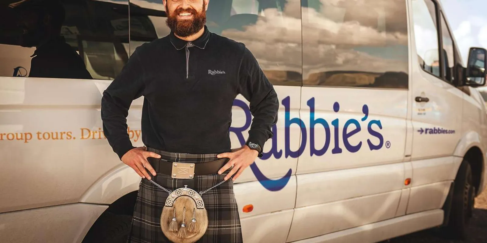 A Rabbie's driver-guide beside the small-group mini-coach used on the Edinburgh day tour